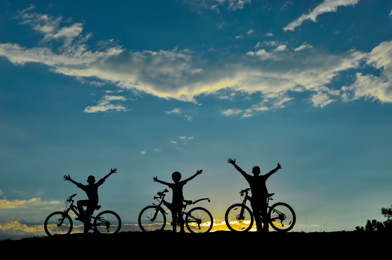 Drei Menschen mit Fahrräder stehen auf einem Bergkamm und strecken die Hände in die Luft.